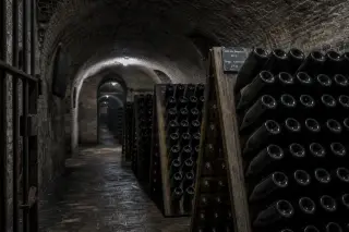 Belgian wine cellar with arched brick vaults and rows of sparkling wine bottles on wooden racks in soft grey light